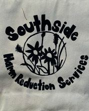 Load image into Gallery viewer, The Circle Tote has a circle in the center of the bag with flowers in the center. The word &quot;Southside&quot; is above the circle and &quot;Harm Reduction Services&quot; is below the circle. Image is on the natural tote. 
